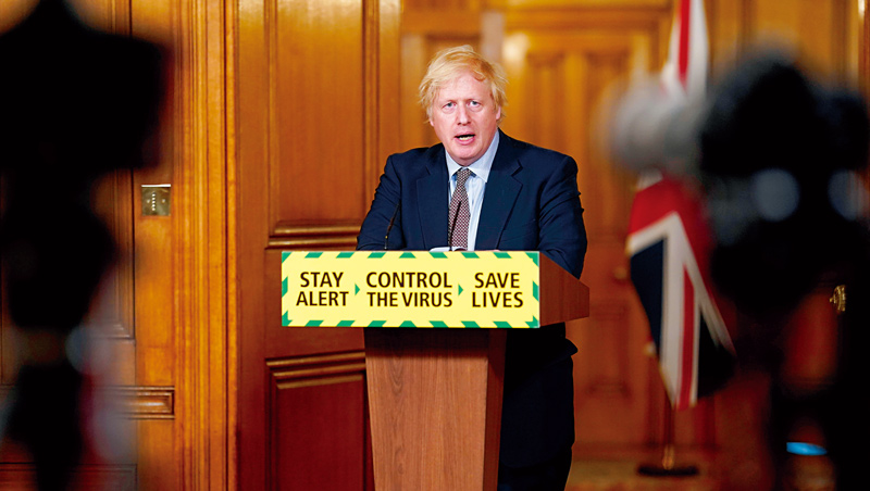 英國首相強森在記者會上向國民更新疫情資訊，演講桌前擺著防疫標語：「保持警覺、控制病毒、拯救性命。」